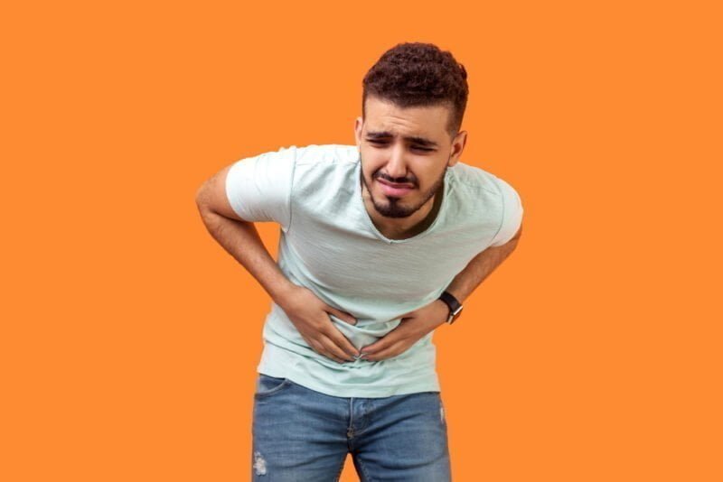 stomachache-portrait-sick-young-man-with-beard-casual-white-t-shirt-grimacing-suffering-from-pain-belly-severe-abdominal-distress-indoor-studio-shot-isolated-orange-background